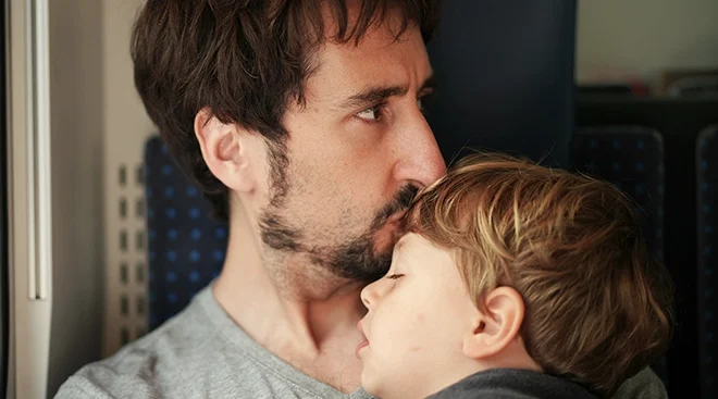 pensive dad kissing toddler's forehead while sitting on a train