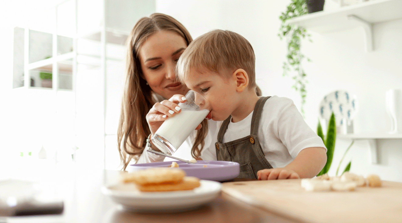 mother giving toddler a glass of milk