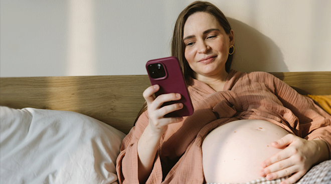pregnant woman relaxing in bed and looking at her phone
