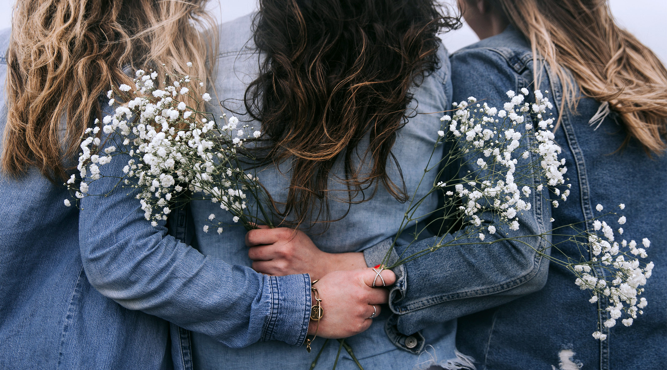 women with their arms around each other and holding white flowers