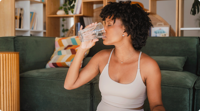 healthy young woman in a workout set at home drinking water
