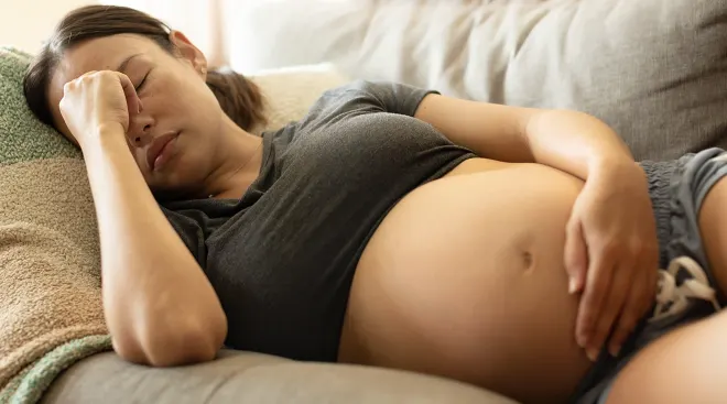 pregnant woman suffering from headache while lying on the couch at home