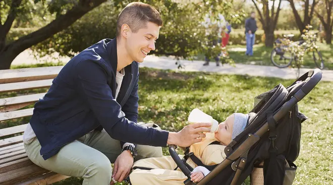 father giving a bottle to his baby in a stroller while at the park