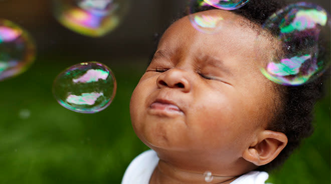Baby with eyes closed outside interacting with bubbles. 