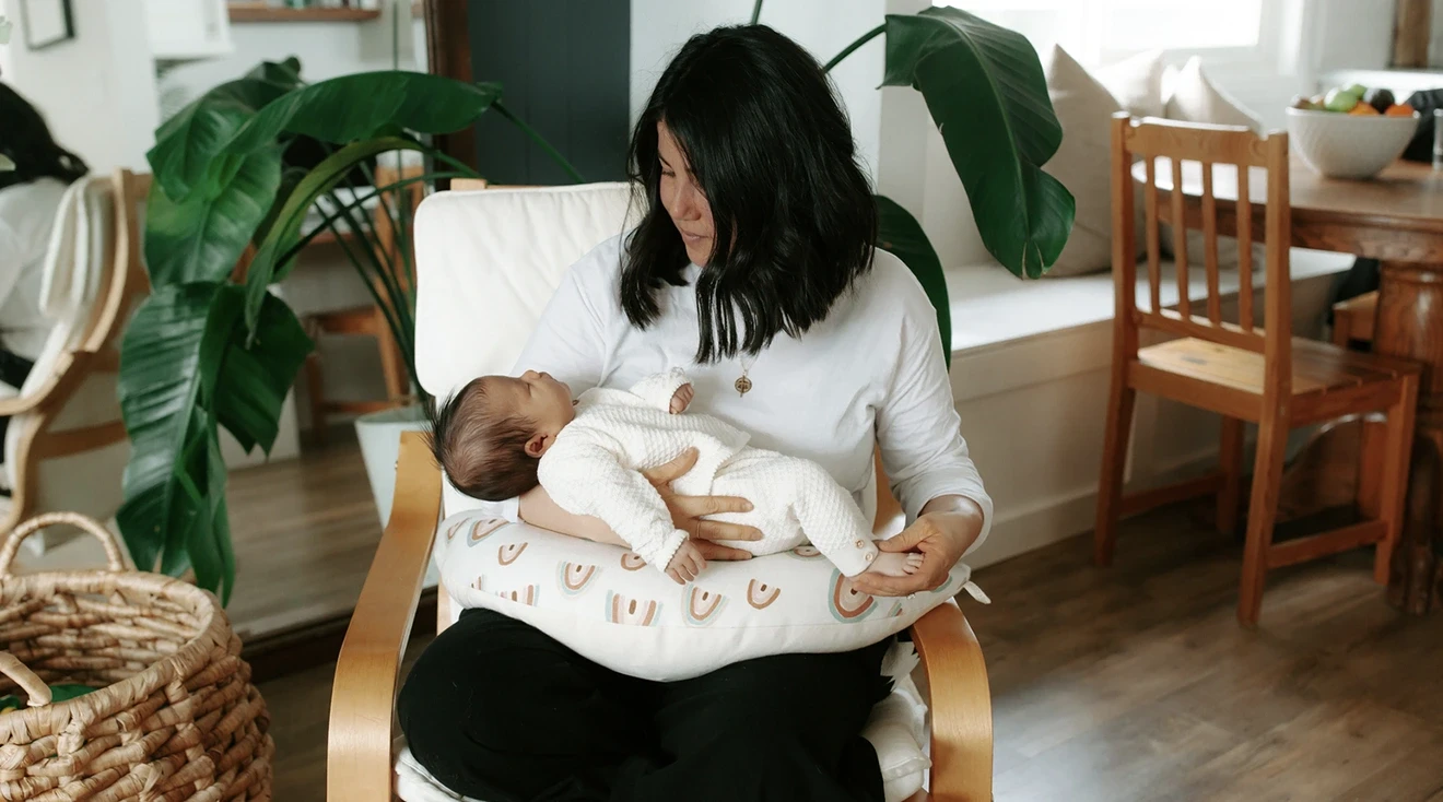 mother holding newborn baby while sitting in chair at home