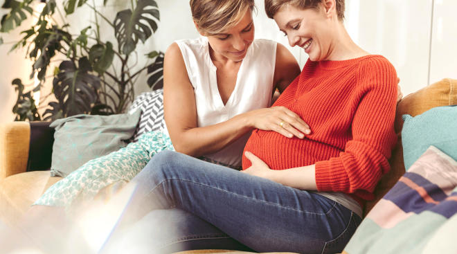 pregnant same sex couple sitting together on the couch at home