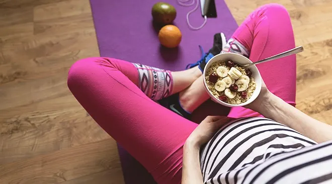 pregnant woman eating oatmeal on workout matt at home