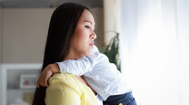 worried mother holding baby while looking out of the window at home