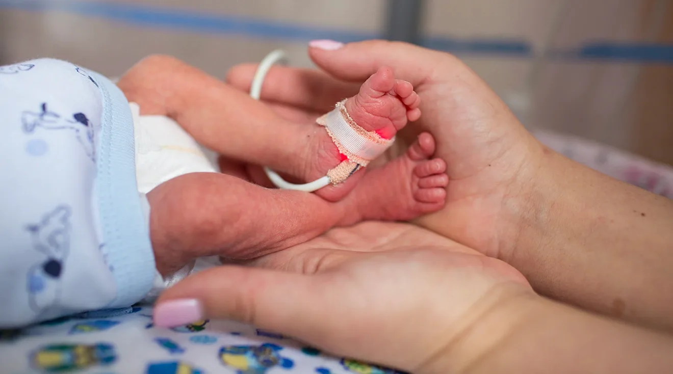 mother holding premature baby's feet while in hospital