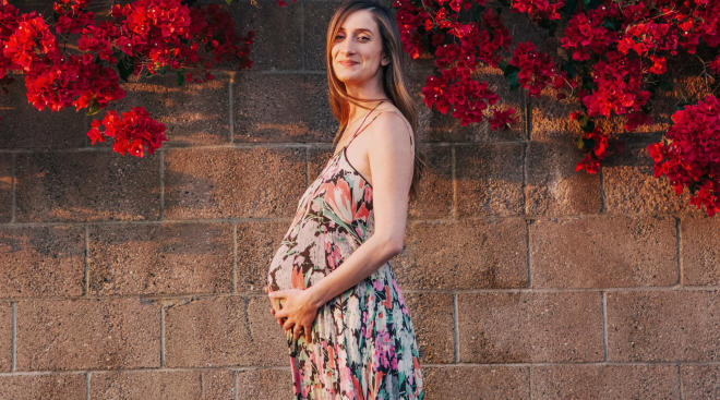 happy pregnant woman pictured outside by a floral wall