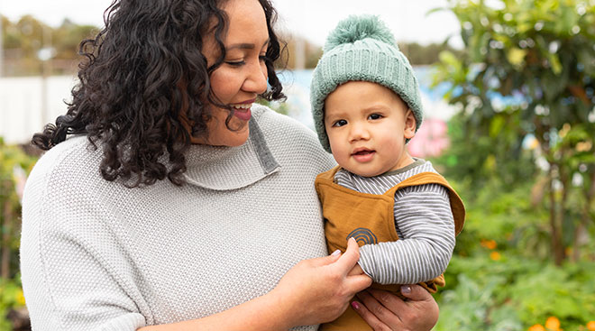 happy mom holds her baby son and tickles his hand, outside in garden