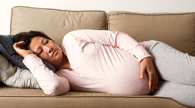 tired and sick pregnant woman lying on couch at home