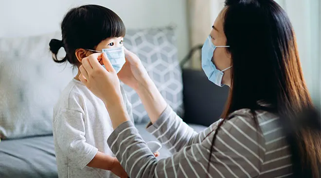 Mom helping her daughter put on a mask.
