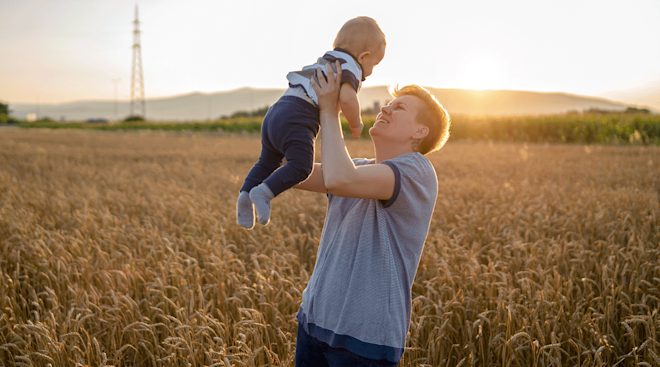 non binary parent holding baby in a field