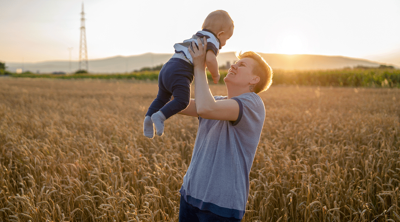 non binary parent holding baby in a field