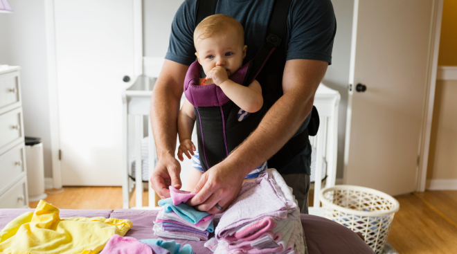 Dad folding laundry with baby in baby carrier