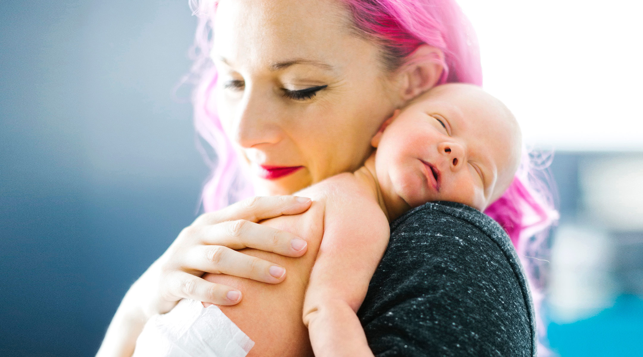 mom with pink hair holds her baby after feeding