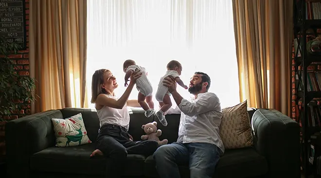 parents holding their twin babies at home on the couch