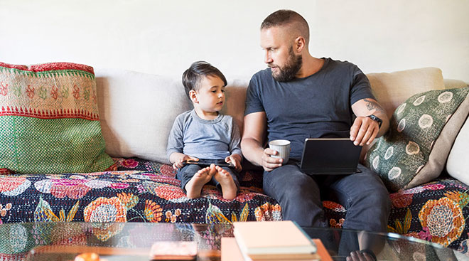 dad helping homeschool his toddler son at home on the couch