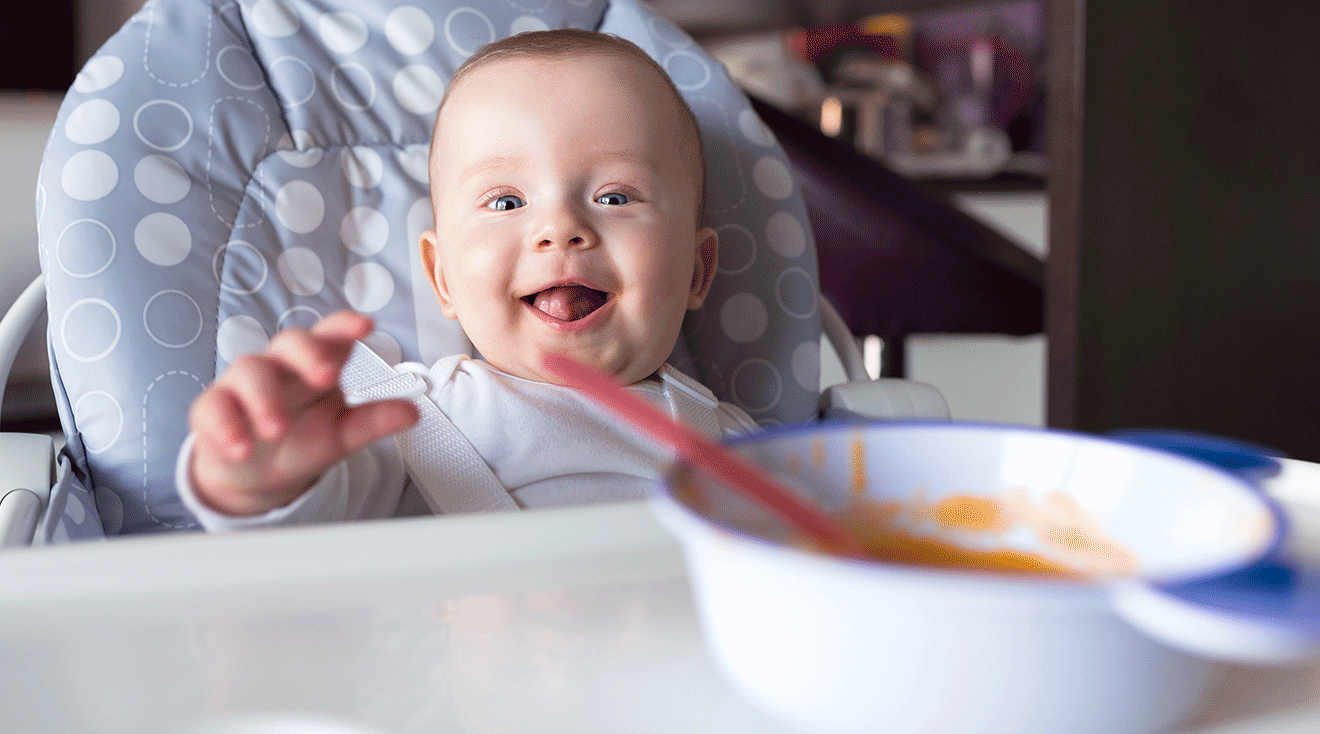 baby eating homemade baby food in high chair at home
