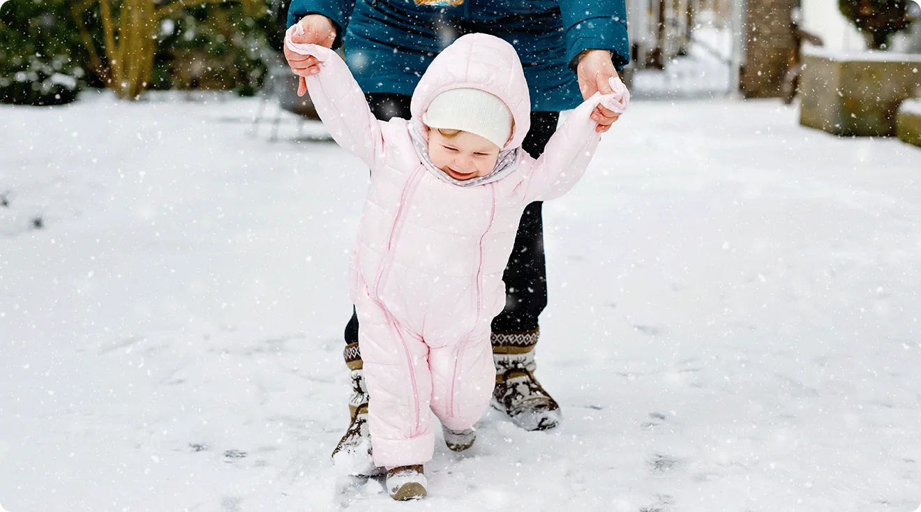 mom walking in the. snow with baby in snowsuit