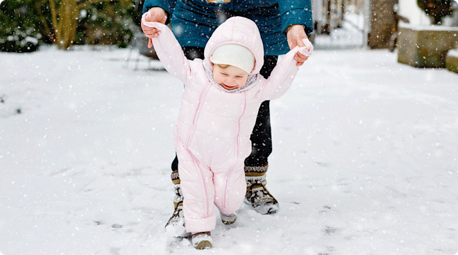 mom walking in the. snow with baby in snowsuit