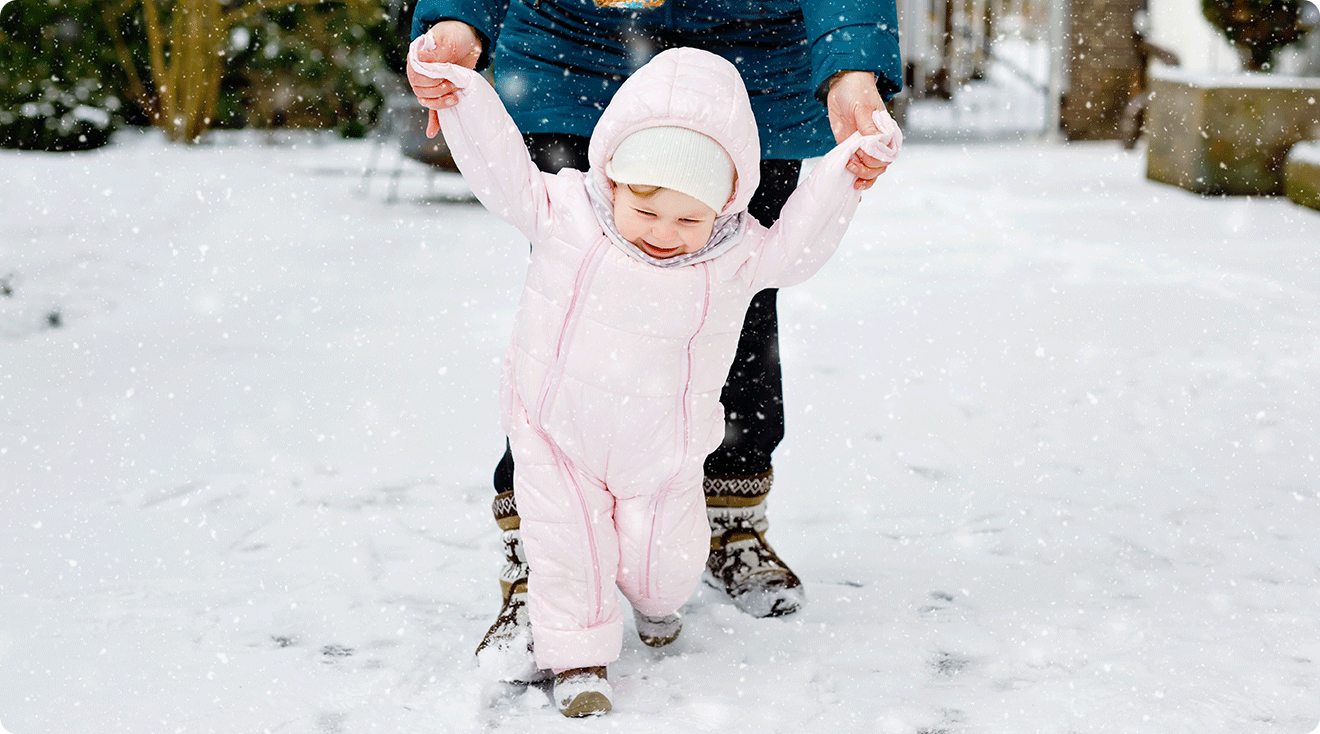 mom walking in the. snow with baby in snowsuit 