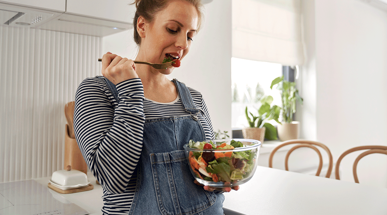 pregnant woman eating a salad in kitchen at home