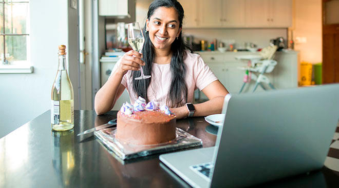 woman celebrates her birthday virtually in her kitchen with a glass of champagne and cake