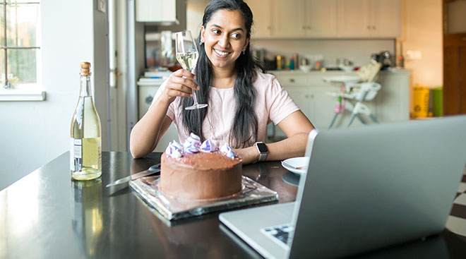 woman celebrates her birthday virtually in her kitchen with a glass of champagne and cake