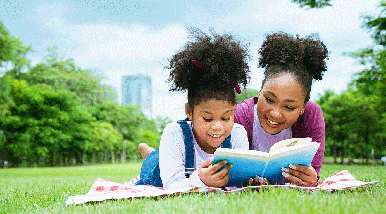 mom and child reading a book outside during summer day