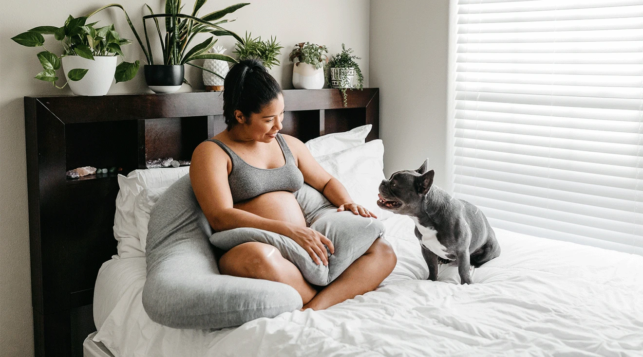 pregnant woman using pregnancy pillow on bed at home