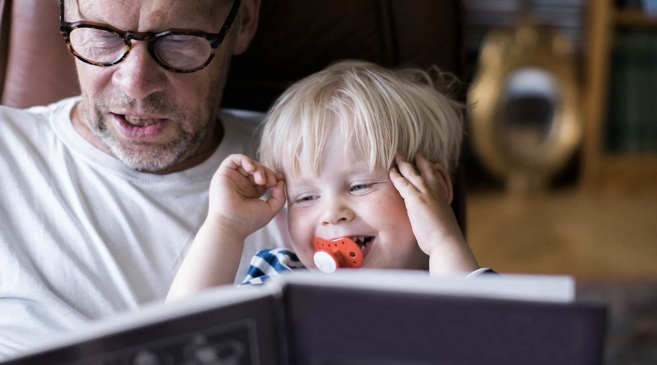 father reading a book with toddler son at home
