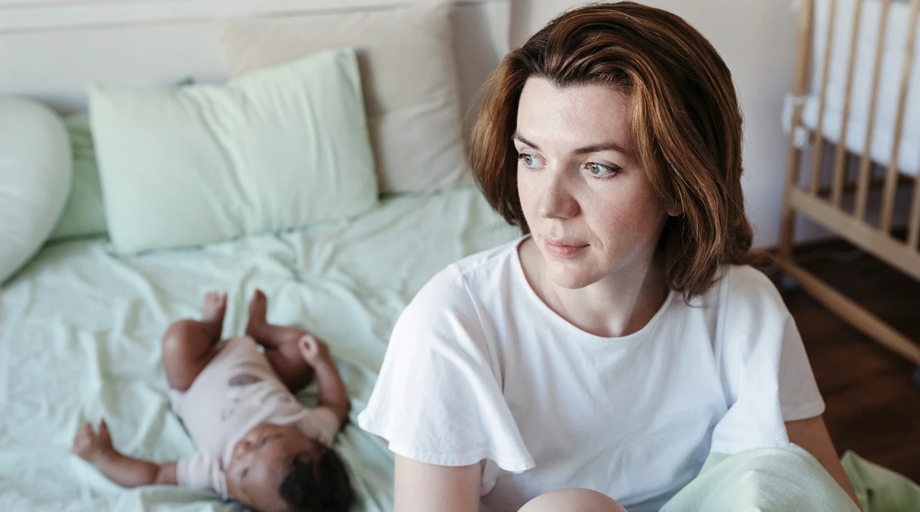 mother pondering while sitting on bed with baby