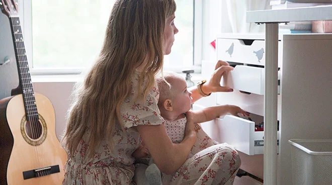 serious mom at home with her baby putting away clothes in a dresser