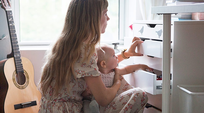 serious mom at home with her baby putting away clothes in a dresser