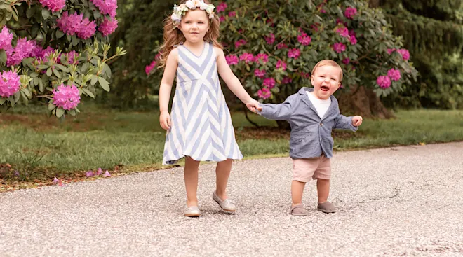 older child playing with toddler outside in gardens