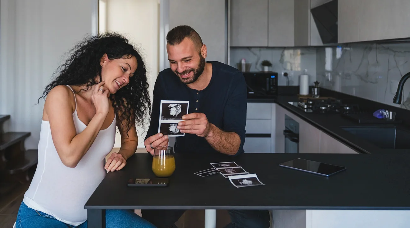pregnant couple sitting in their kitchen looking at ultrasound photos