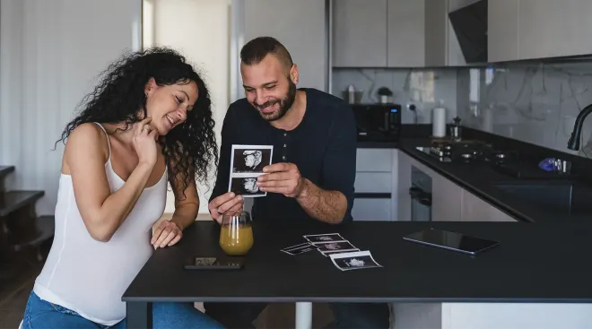 pregnant couple sitting in their kitchen looking at ultrasound photos