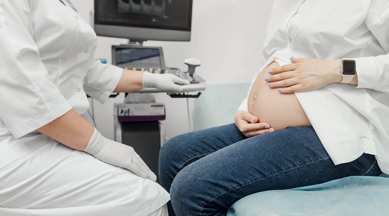 pregnant woman sitting on exam table while talking to doctor