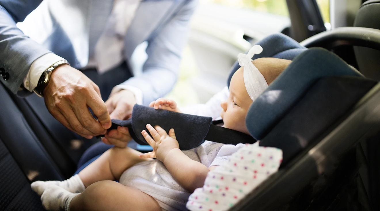 father buckling baby into car seat in the car