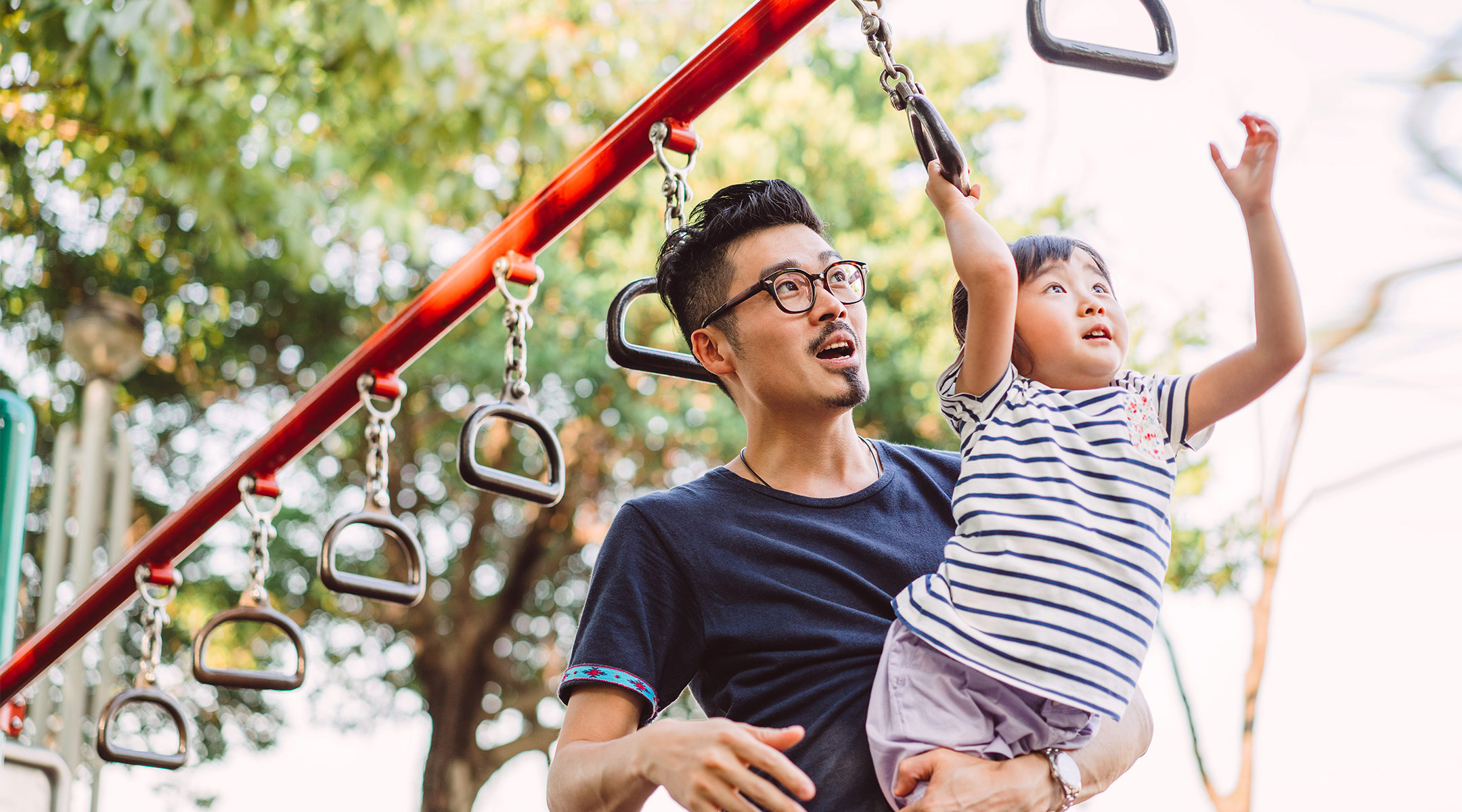 dad helps young daughter on the monkey bars at the playground