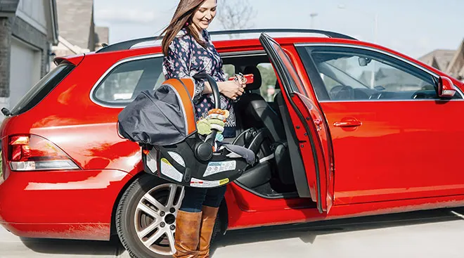 mom holding car seat about to put baby in her red car