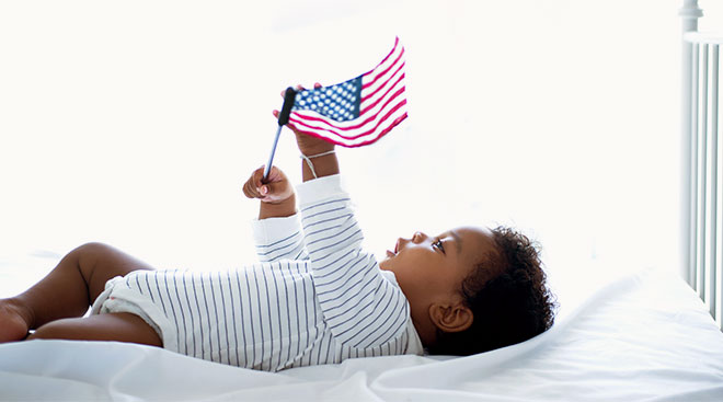 baby lying in crib holding an american flag