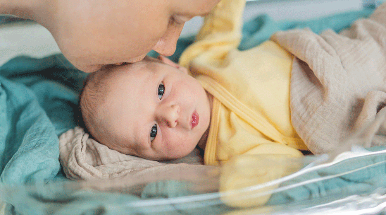 woman kissing newborn baby's head in hospital