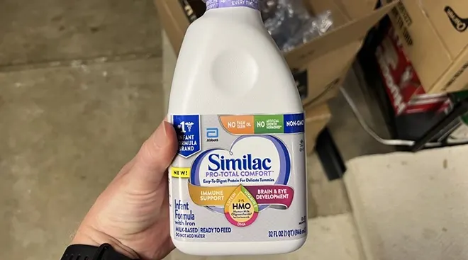 Person's hand holding Similac baby formula from Abbott Laboratories above shipment boxes in Lafayette, California, May 13, 2022