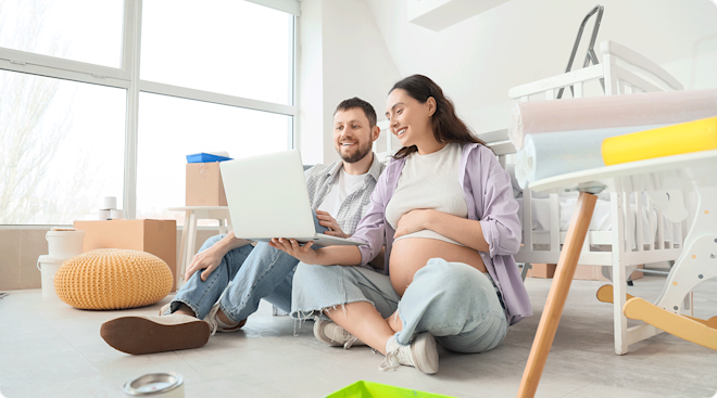 pregnant couple looking at baby registry on laptop while sitting in baby nursery