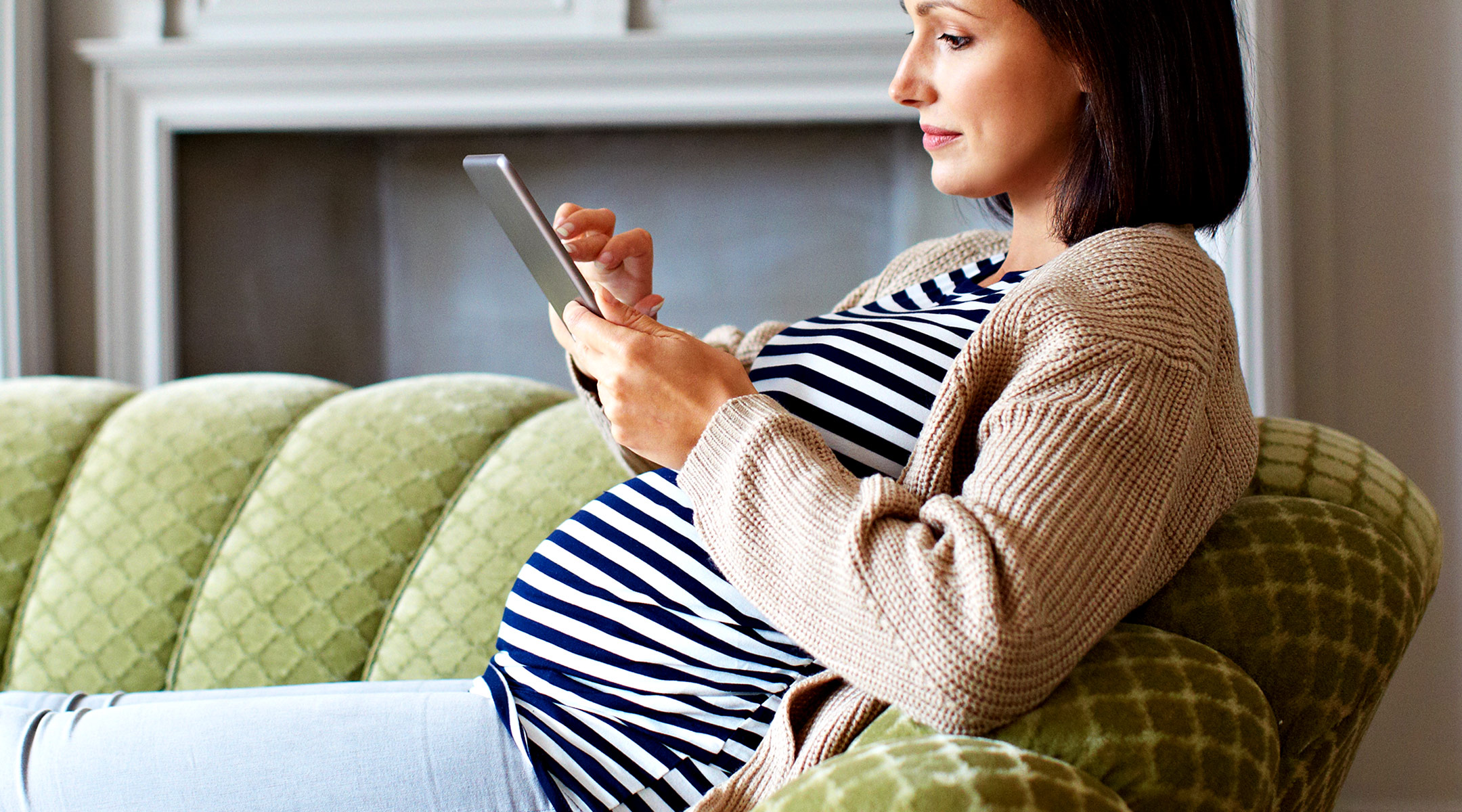 pregnant woman sitting on couch using tablet