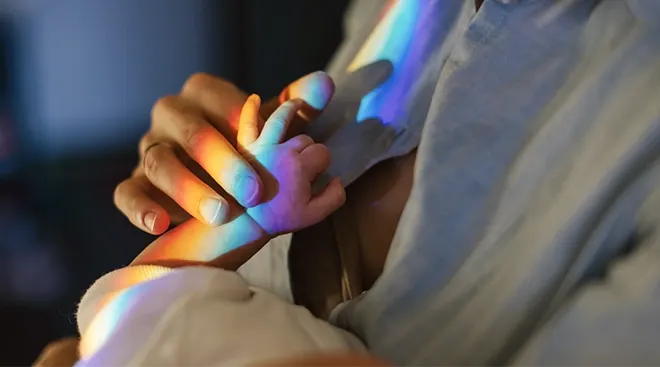 mother holding baby's hand with rainbow light reflected on them