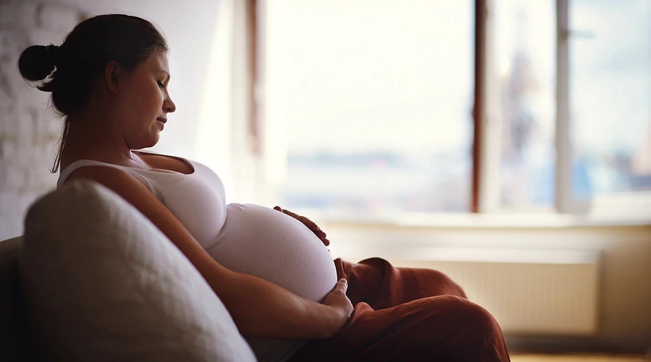 pregnant woman relaxing on couch at home; sore and tender breasts during pregnancy